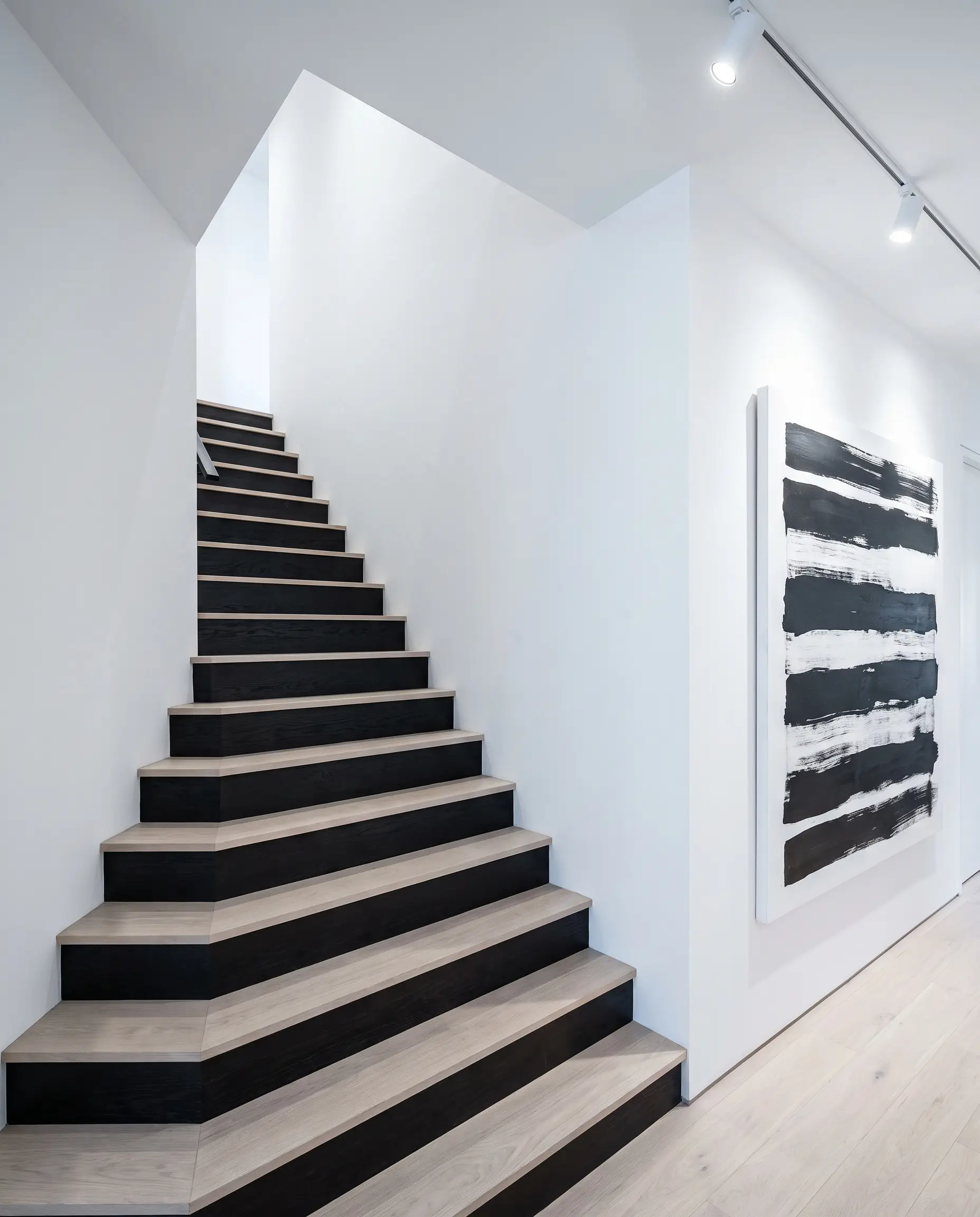 Opaque pitch-black ebonized wood vertical risers pair with pale bleached oak horizontal treads in a minimalist hallway embodying 2027 staircase and railing trends.