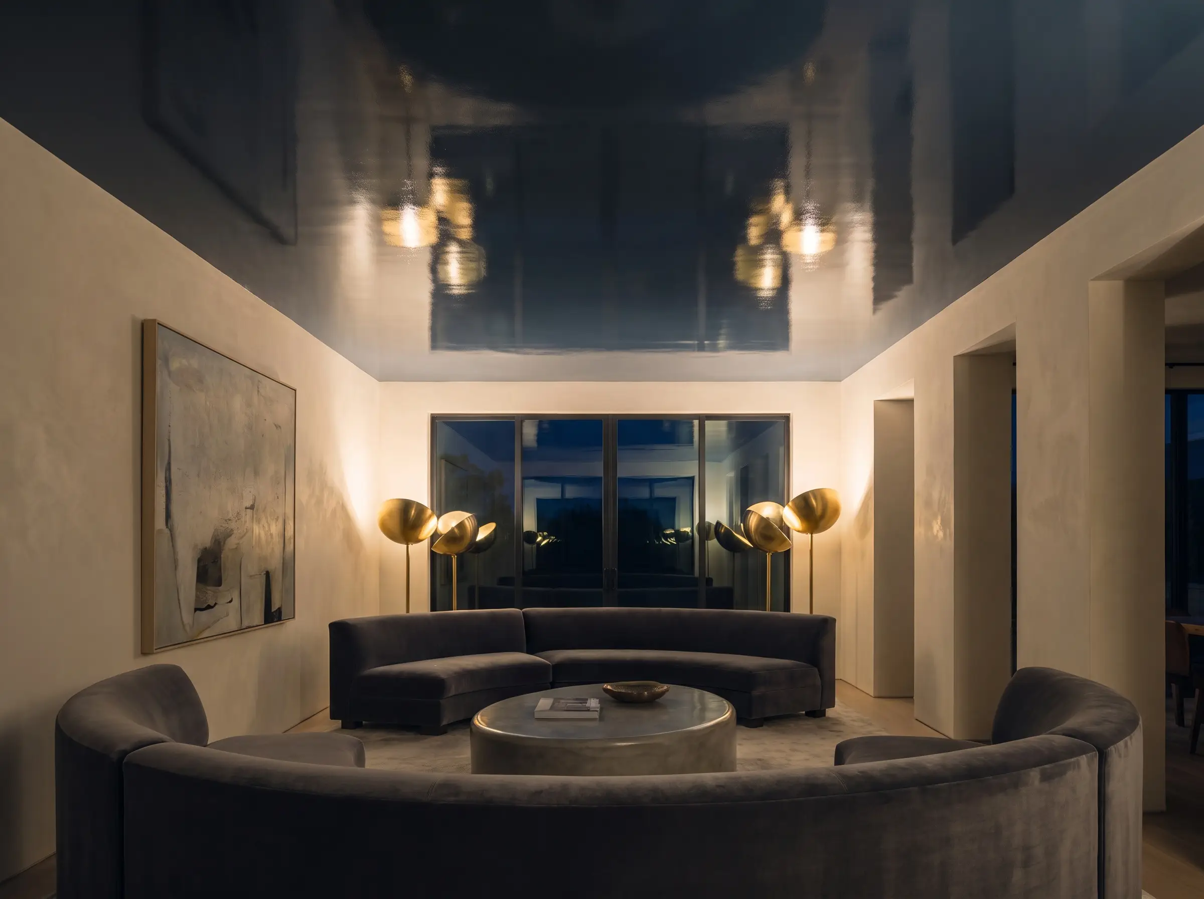 A dramatic fifth wall lacquered in a high-gloss Benjamin Moore Hale Navy finish reflects upward-casting floor lamps above soft plaster walls and low-profile seating.
