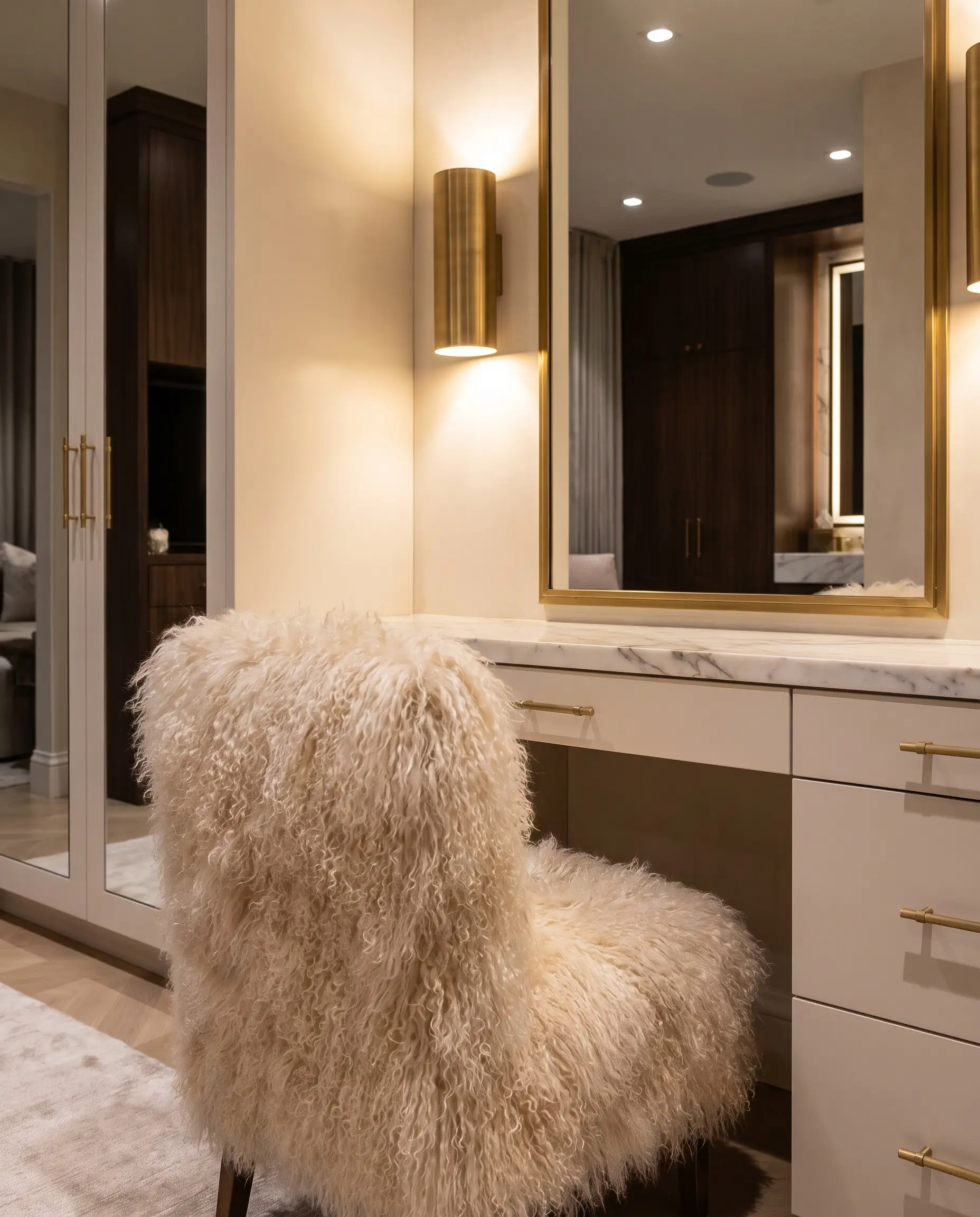 Tabouret de coiffeuse tapissé de mohair de chèvre angora à poil long sous des appliques en laiton brossé près d'une vasque en marbre.