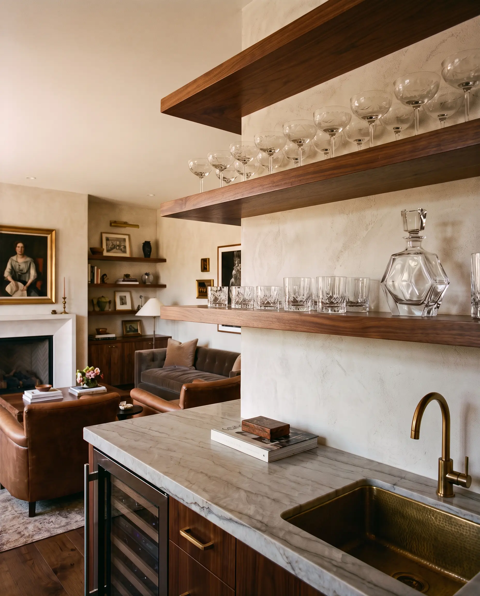 Vintage etched-glass coupes and a geometrically distinct crystal decanter sit on elegant wood open shelving above a beautiful stone countertop in a functional entertaining zone.