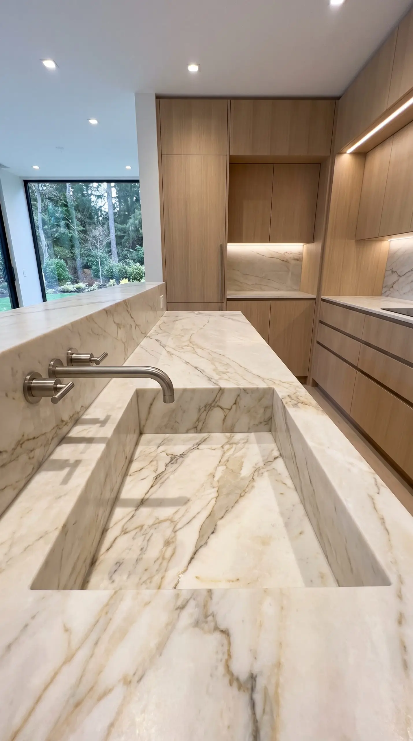 A heavy-duty integrated stone basin constructed entirely from heavily veined Taj Mahal quartzite sits beneath a minimalist brushed nickel wall-mounted faucet.