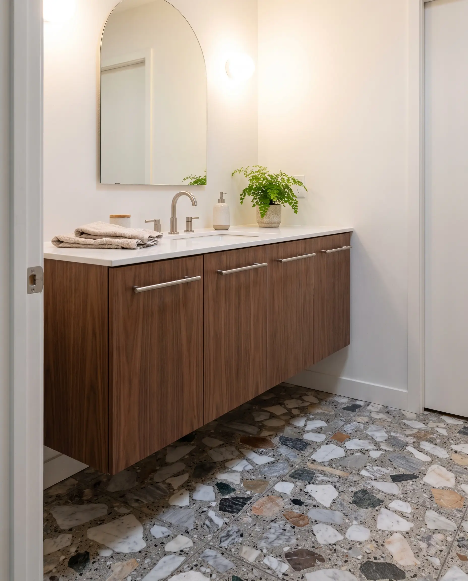 Un autentico pavimento in seminato veneziano con graniglia di marmo irregolare accoglie un mobile bagno in noce canaletto, rubinetteria in nichel spazzolato e specchio ad arco.