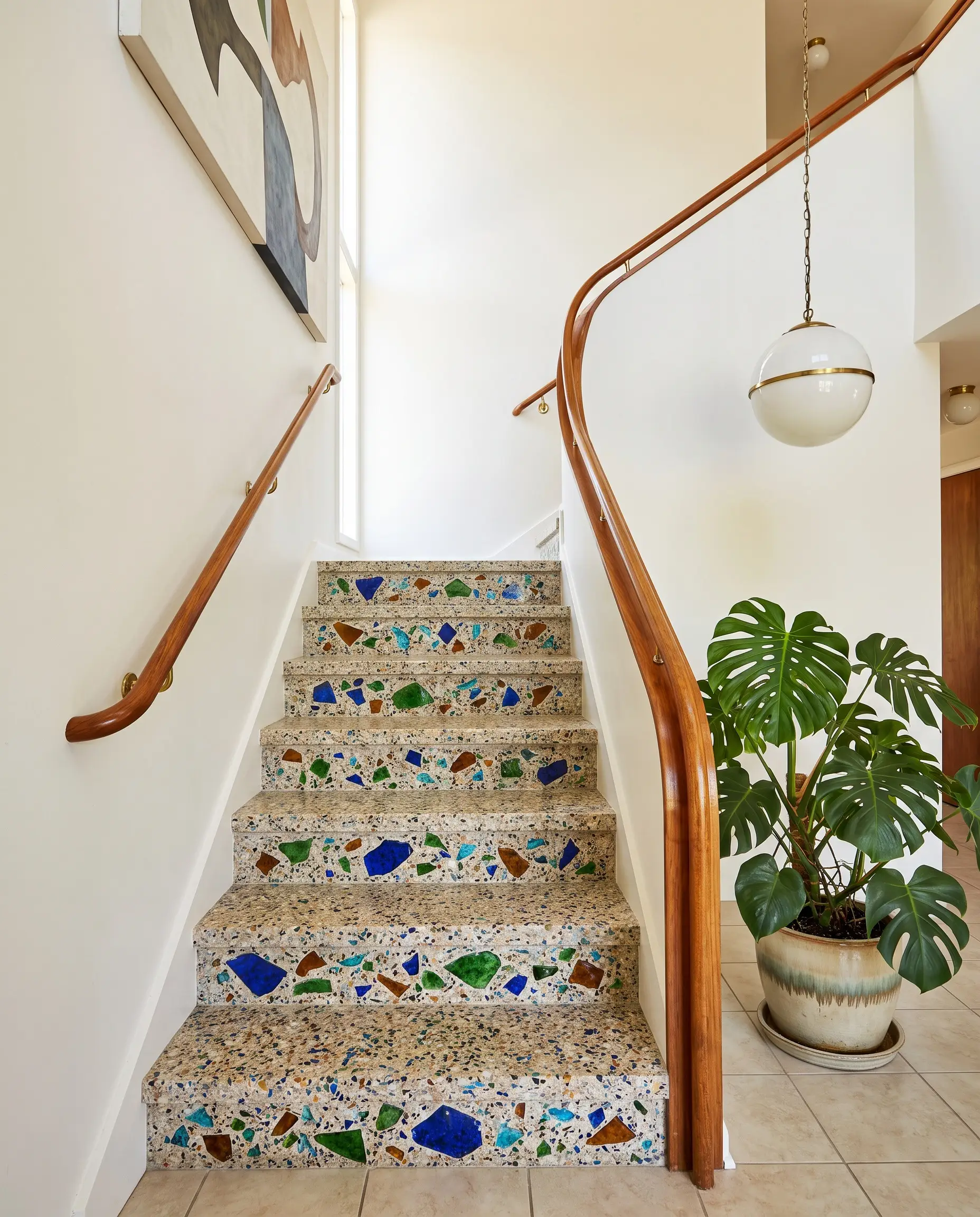 Custom pre-cast terrazzo stair treads loaded with recycled glass aggregate are flanked by a sleek curved wooden handrail and a crisp white wall.