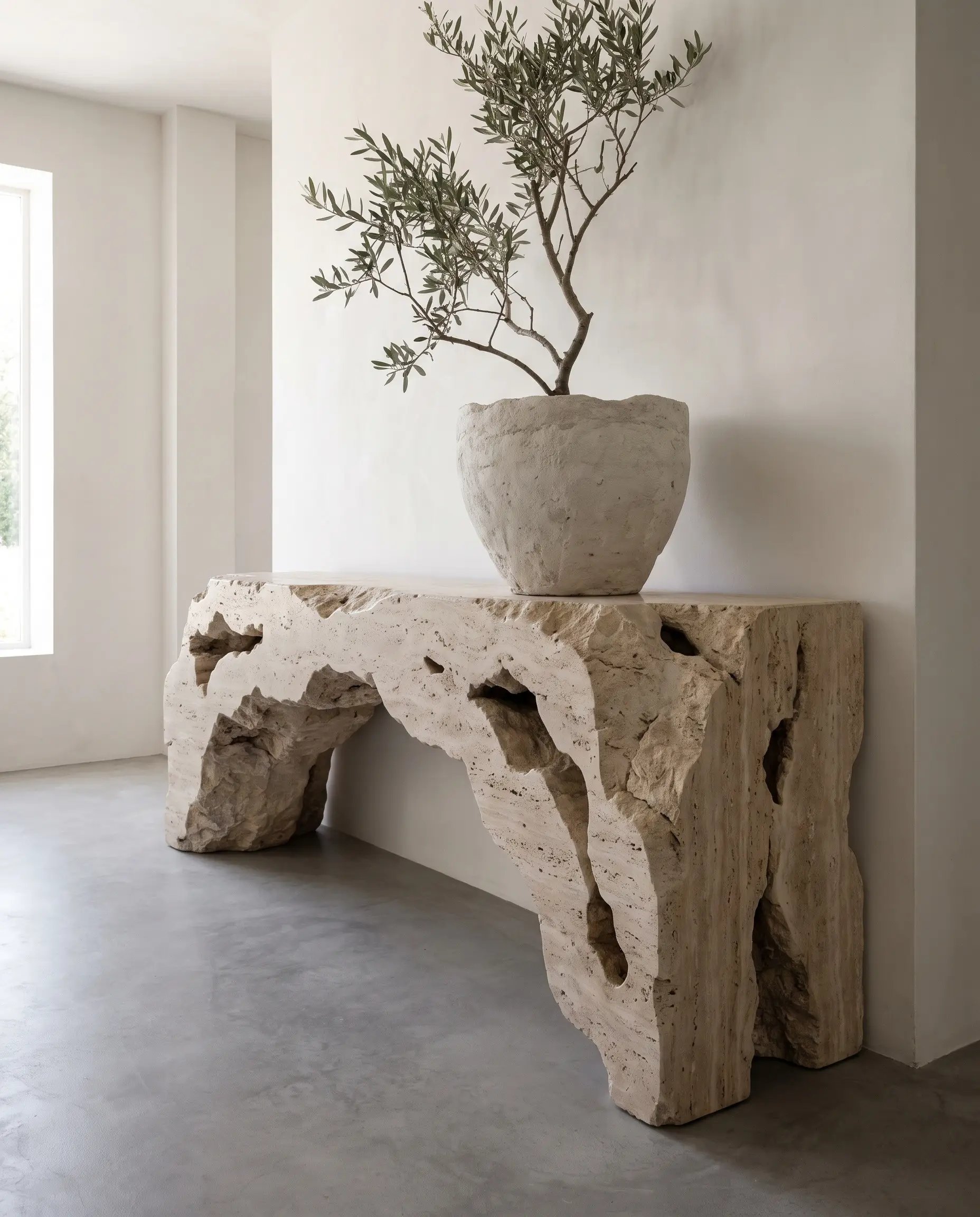 A heavy curvilinear console table carved from raw travertine with a waterfall edge anchors a smooth plaster wall in these 2027 entryway and mudroom design trends.
