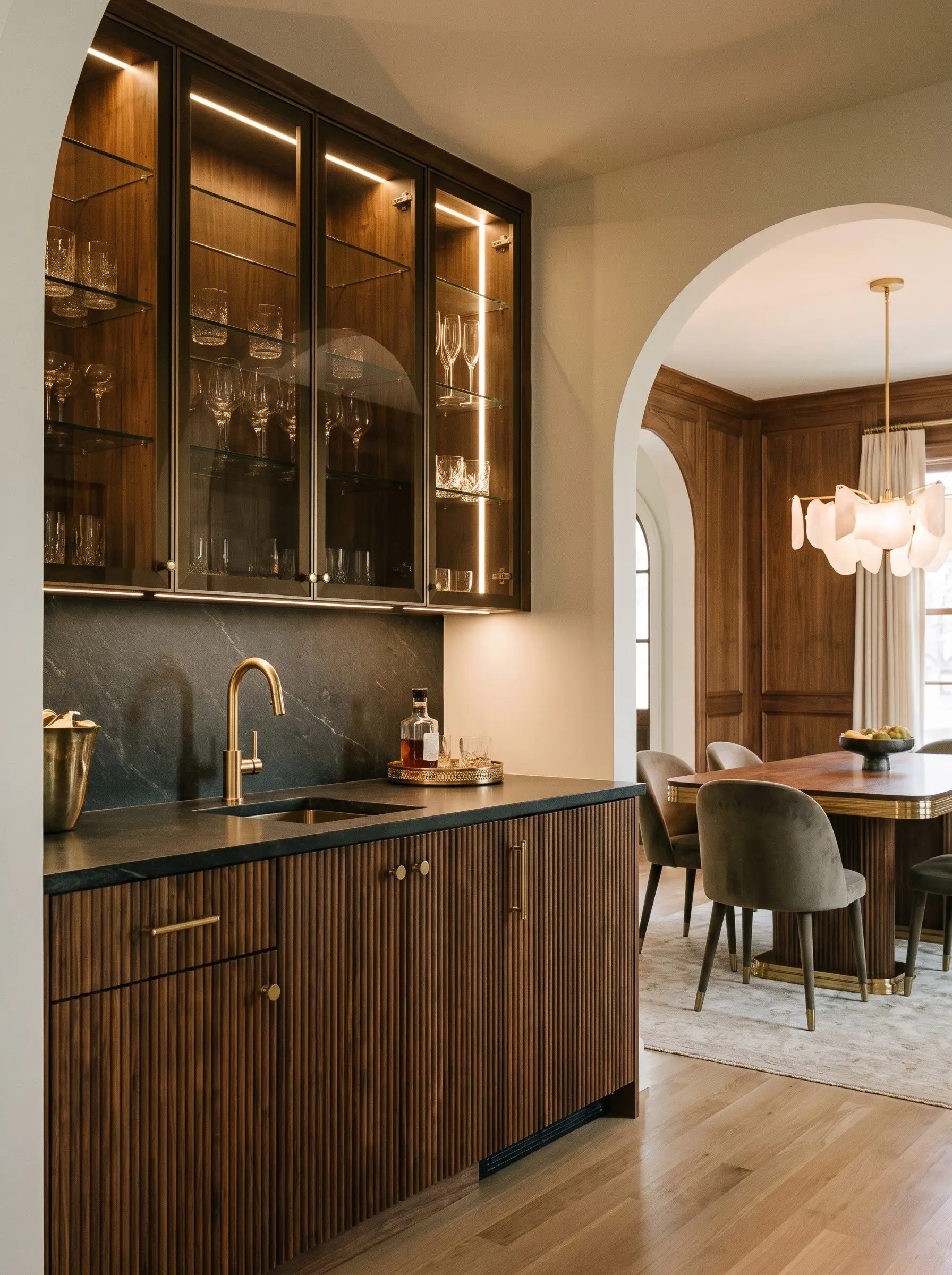 Bronze smoked glass upper cabinets pair with warm reeded walnut base cabinets and a sleek stone countertop in this art deco revival dining area.