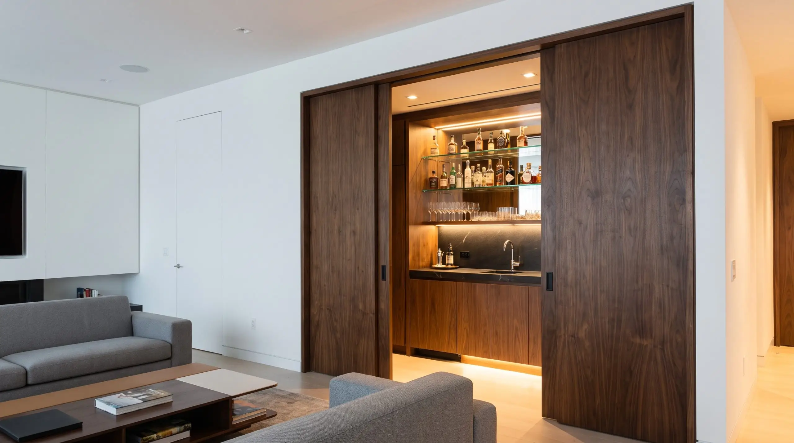 Heavy-duty retractable pocket doors reveal a fully stocked walnut veneer wet bar integrating home bar and wine storage trends into a minimalist living room.
