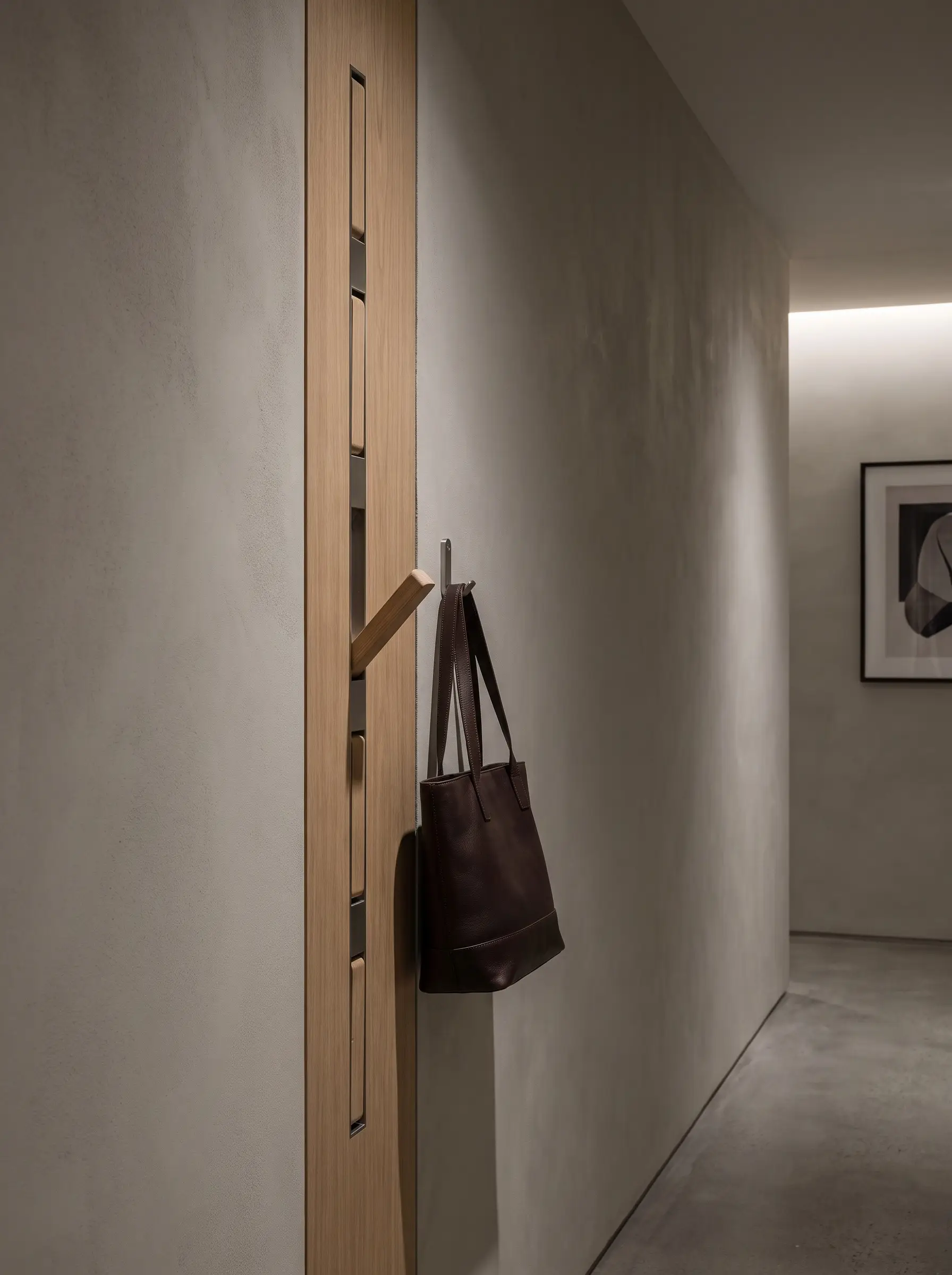 Custom retractable marine-grade stainless steel coat hooks fold perfectly flat into a milled white oak vertical panel, holding a structured leather tote.