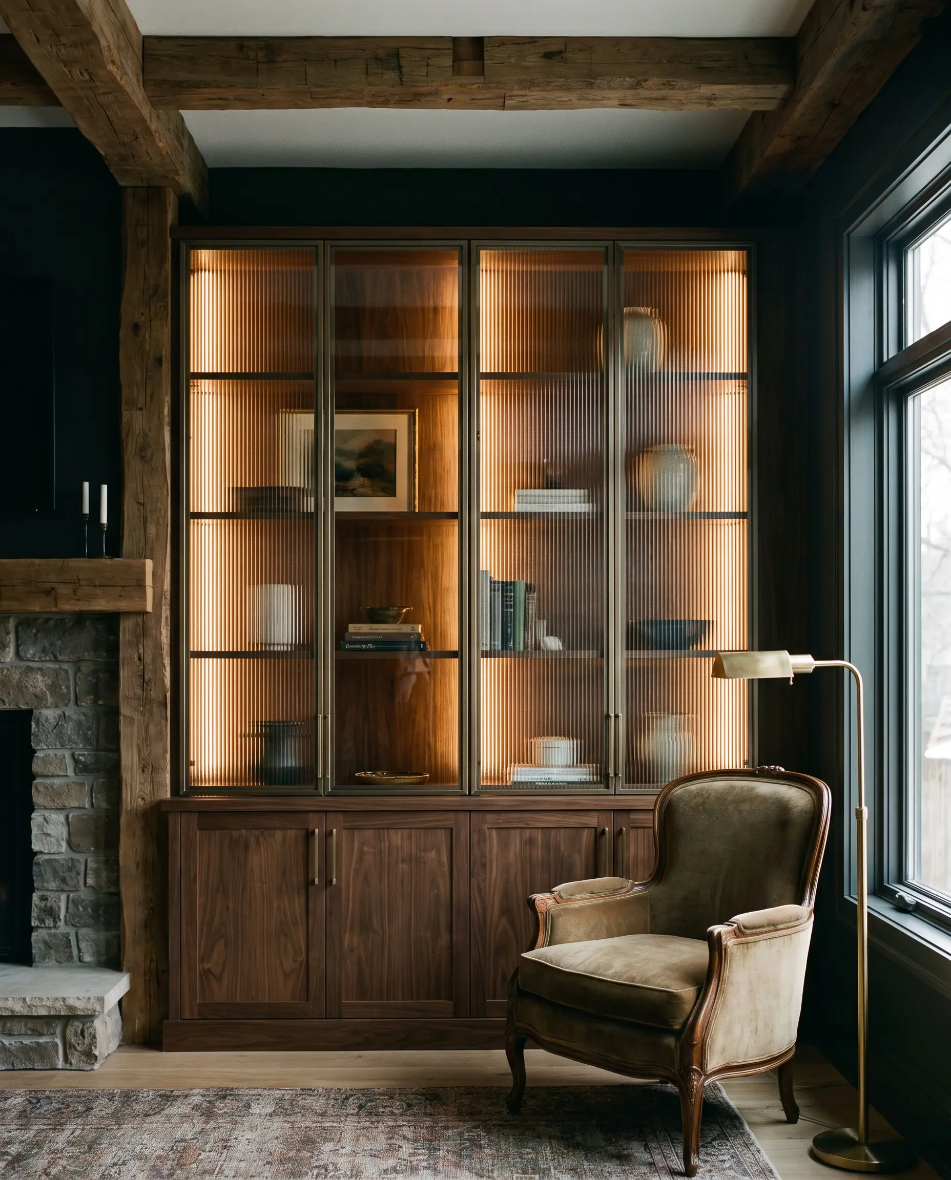 Custom millwork cabinet doors featuring heavy ribbed fluted glass and smoked bronze accents obscure curated objects next to a comfortable reading chair.