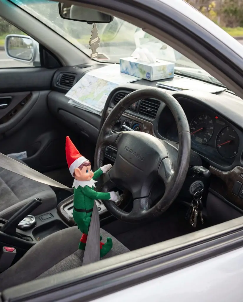 Un elfo di Natale allacciato con la cintura di sicurezza al posto di guida dell'auto di famiglia con le mani sul volante.