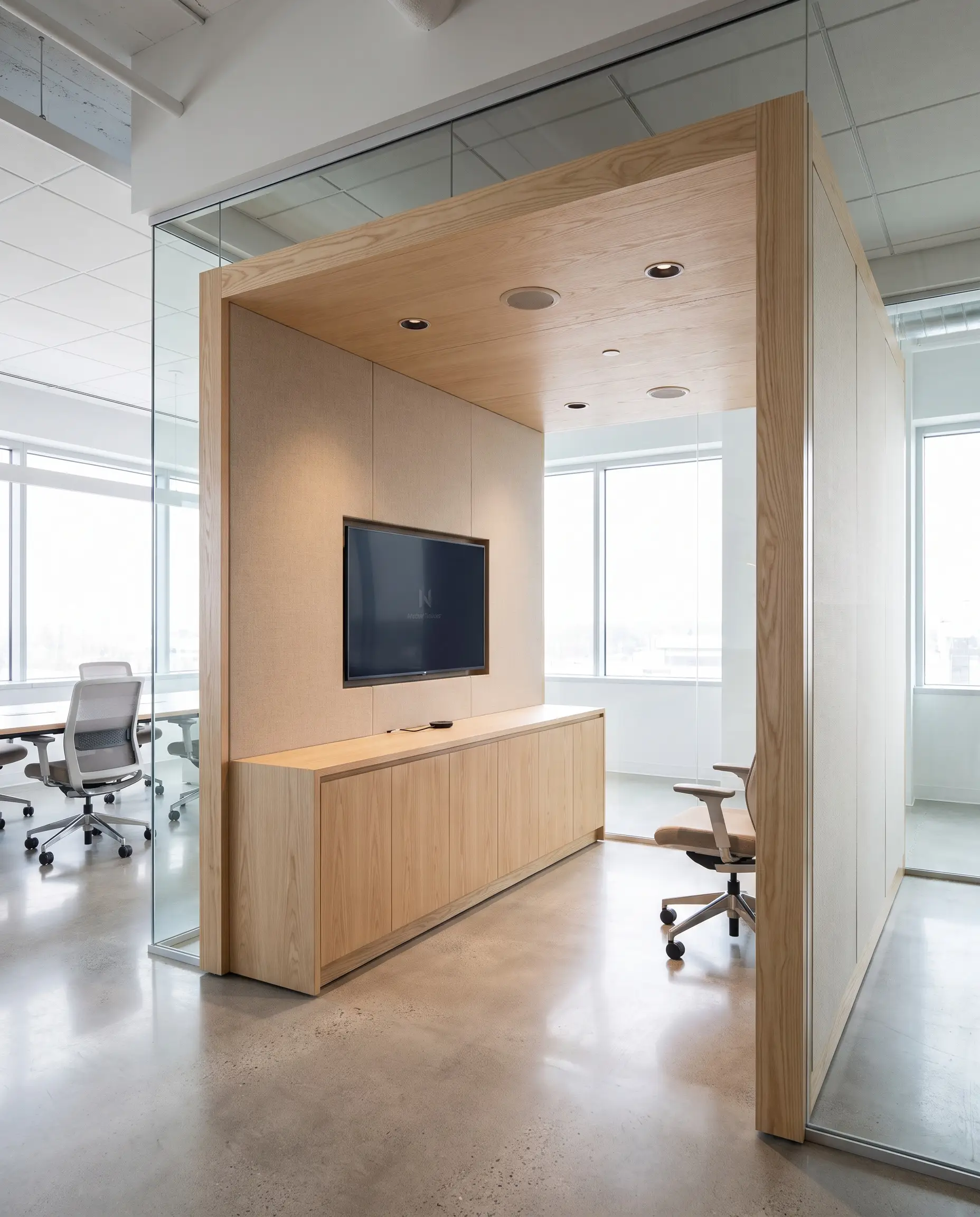Solid ash millwork and acoustically transparent fabric panels conceal a flush-mounted digital screen and hidden cables within this hybrid communication pod.