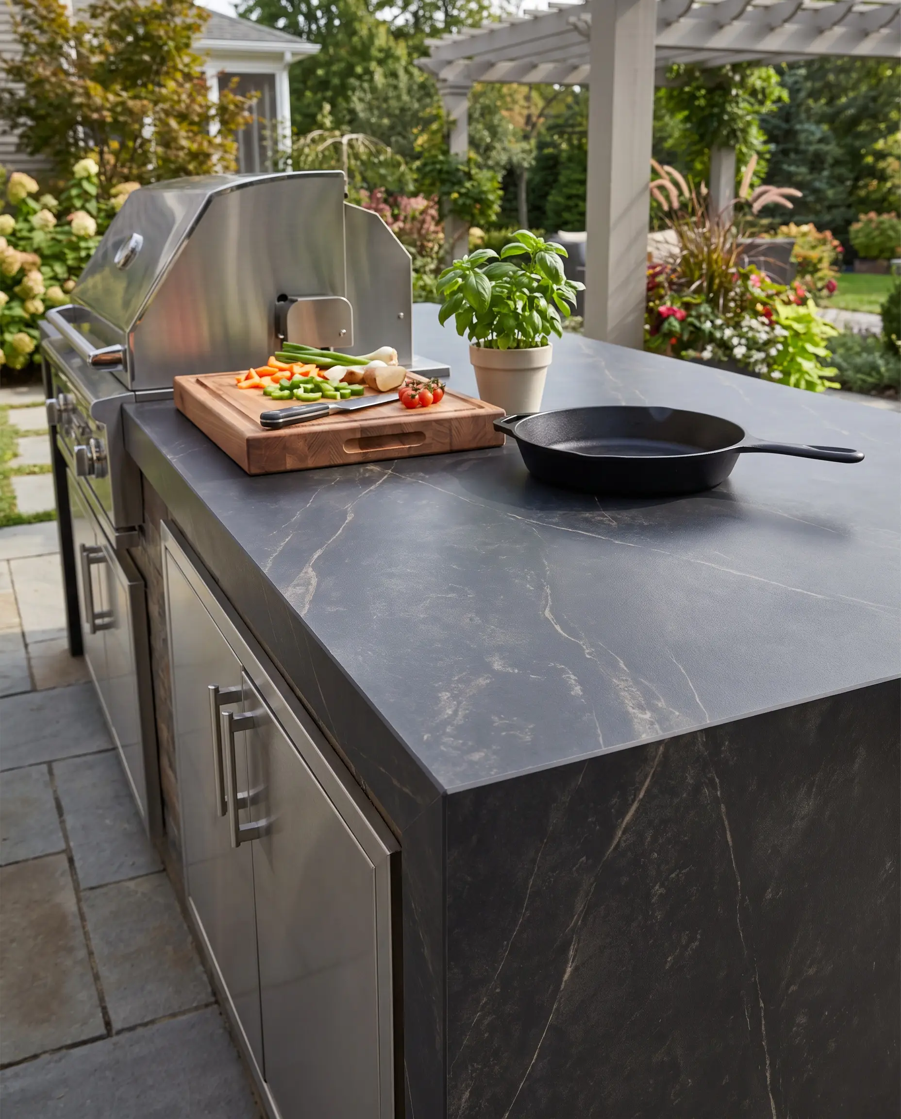 Piano di lavoro in pietra sinterizzata da 20 mm montato su mobili outdoor in acciaio inox con tagliere in legno e padella in ghisa.