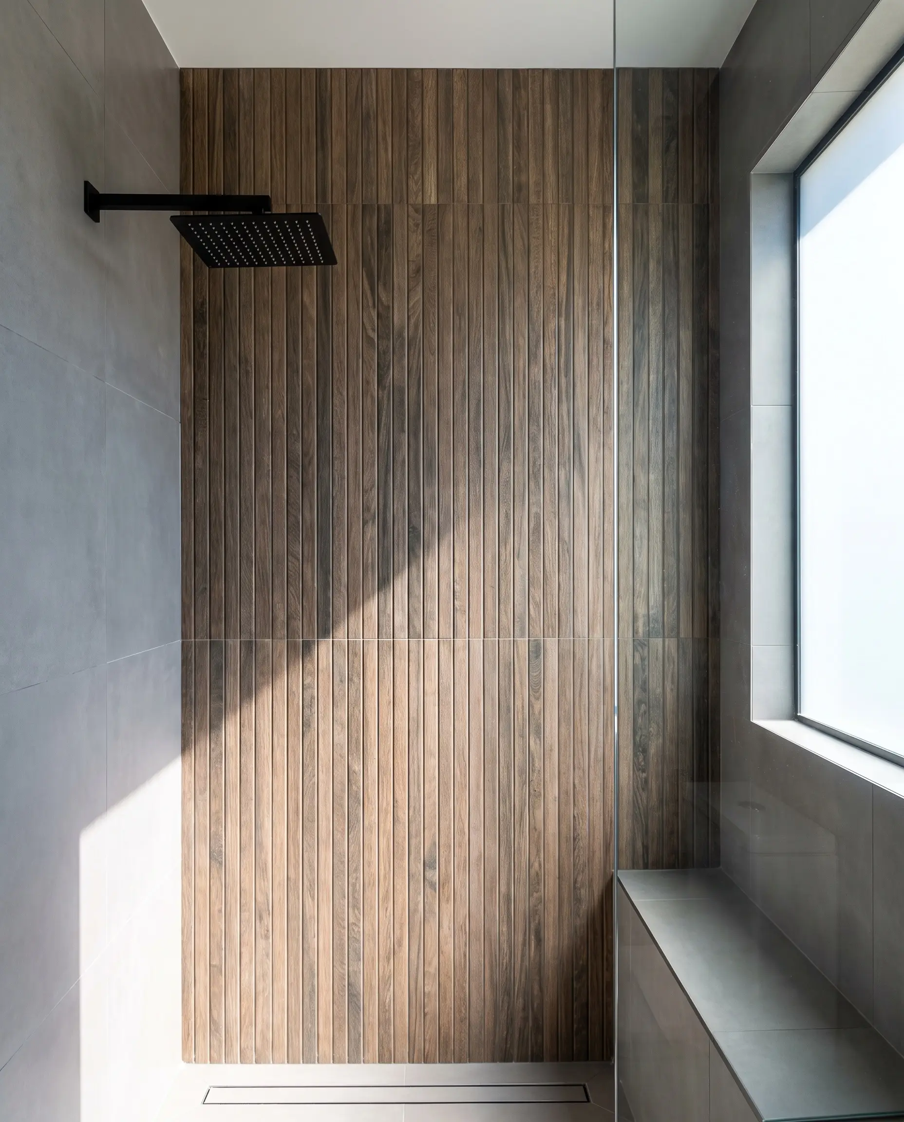 Hyper-realistic slatted wood-look extruded porcelain tiles with rectified edges create a vertical timber cladding illusion beside smooth matte gray wall tiles.