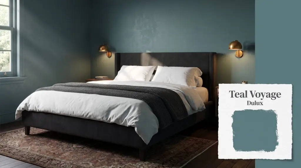 A dark charcoal upholstered bed and brass wall sconces are positioned against deep teal walls coated in Dulux Teal Voyage (Hex #5A8487).