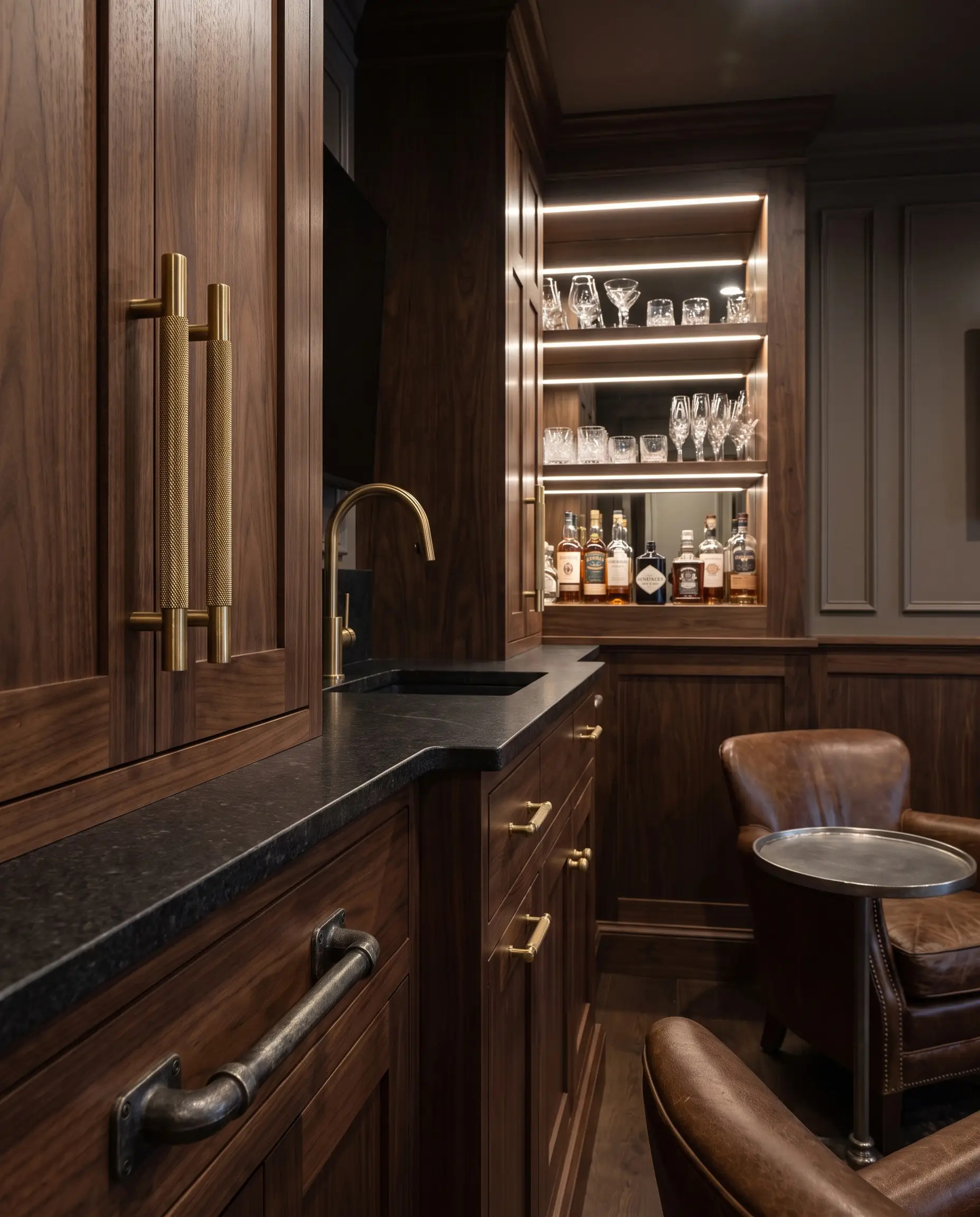 Heavy knurled unlacquered brass and gunmetal hardware pulls accent deep-toned custom cabinetry alongside a matching brass faucet and natural stone countertop.