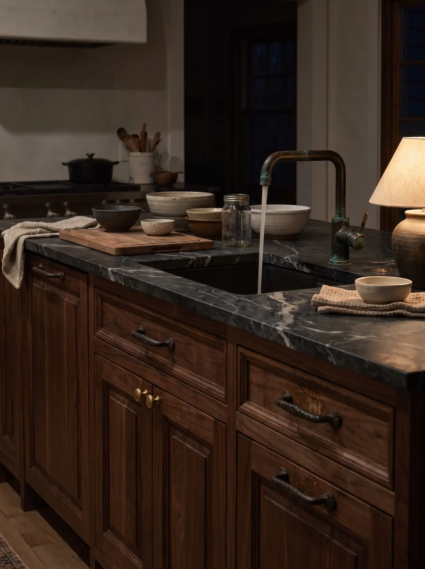 Heavily articulated European walnut kitchen cabinetry is accented with unlacquered brass hardware, a dark oil-rubbed bronze faucet, and a heavily veined honed soapstone countertop.